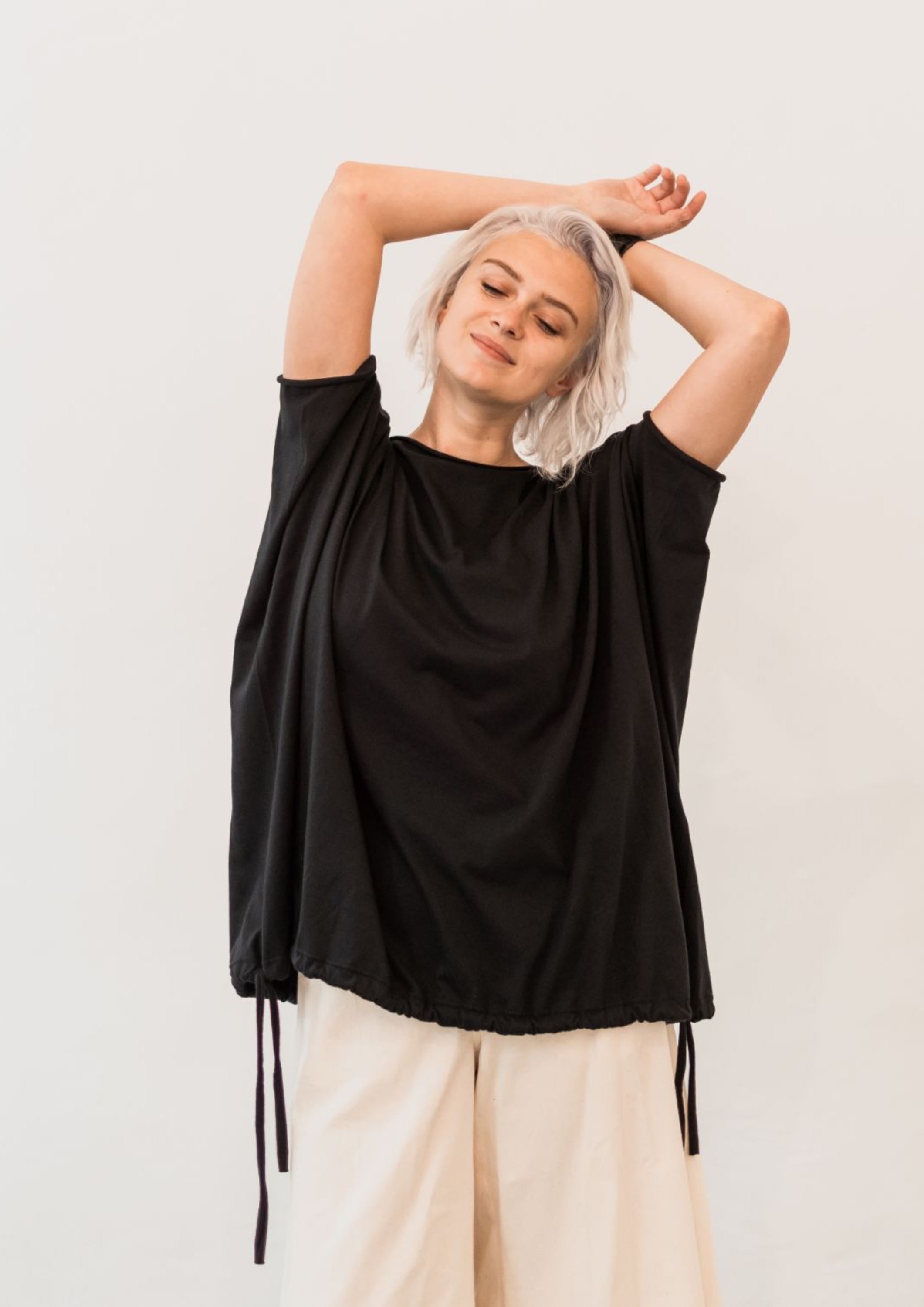 Multifunctional black fluid jersey, made from 100% organic cotton. Can be worn as a blouse, vest or poncho. With two sided adjustable drawn strings. 